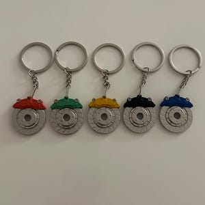 May include: Five silver brake rotor keychains with different colored brake calipers. The calipers are red, green, yellow, black, and blue.