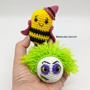 Op de afbeelding: Twee gehaakte pluche speelgoedjes. Eén is een gele en zwarte bij met een roze hoed. De andere is een wit monster met groen haar en paarse ogen.  @MON.AMI.CROCHET