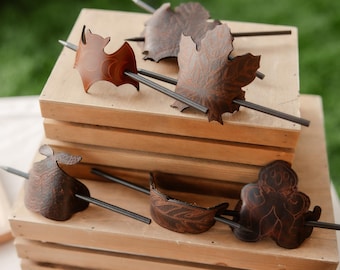 Könnte beinhalten: Eine Sammlung handgefertigter Haaraccessoires, darunter Spangen und Haarstäbe. Die Spangen sind wie eine Fledermaus, ein Blatt und andere organische Formen geformt. Sie sind aus dunkelbraunem Leder gefertigt und haben einen Metallstab.