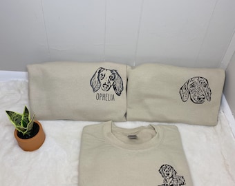 May include: Three beige sweatshirts with black dachshund dog illustrations and names "Ophelia", "Martha" and a third name that is unclear.