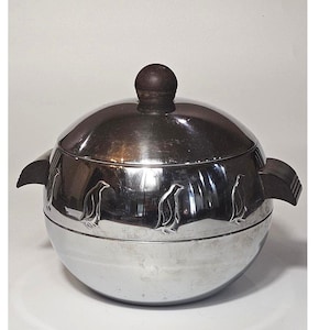 May include: A silver-toned ice bucket with a lid and dark wooden handle and knob. The bucket features embossed penguin designs around the base. The lid has a dark wooden knob. The bucket has two dark wooden handles on either side.