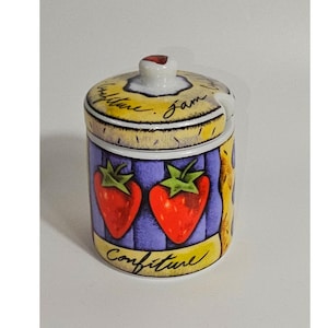 Puede incluir: Un tarro de mermelada de cerámica con tapa, decorado con dos fresas rojas sobre un fondo morado. La tapa tiene un pequeño asa y el texto "Confiture" y "Jam" escrito en negro. La base también presenta la palabra "Confiture" en letras negras.