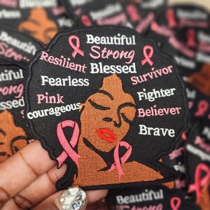 May include: Black and pink embroidered patch with a woman's face and the words "Beautiful Strong Resilient Blessed Survivor Fighter Believer Brave" and "Pink courageous".