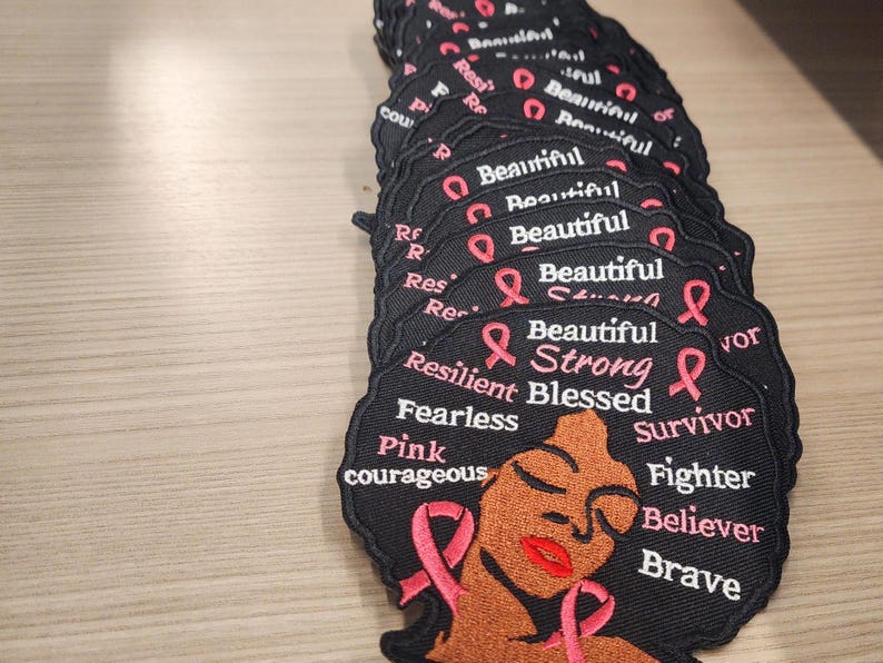 May include: Black and pink embroidered patch with a woman's face and the words "Beautiful Strong Blessed Survivor Fighter Believer Brave" and "Resilient Fearless Pink Courageous".