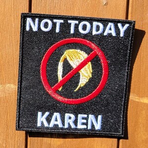 May include: A black patch with white text that says "NOT TODAY KAREN". A red circle with a diagonal line through it is in the center of the patch. Inside the circle is a yellow silhouette of a woman's hair.