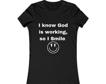 Pode incluir: Camiseta preta para mulher com texto branco que diz "Eu sei que Deus está trabalhando, então eu sorrio" e um rosto sorridente branco com cílios.
