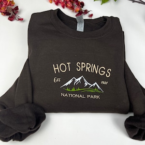 May include: Brown sweatshirt with a white embroidered design that says "HOT SPRINGS Est. 1921 NATIONAL PARK" with a green mountain range graphic.