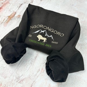 May include: Black sweatshirt with a white embroidered design that says "NGORONGORO Est. 1959 CONSERVATION AREA" with a mountain range and a lion in the center.