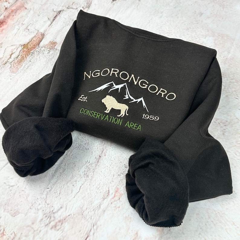 May include: Black sweatshirt with a white embroidered design that says "NGORONGORO Est. 1959 CONSERVATION AREA" with a mountain range and a lion in the center.