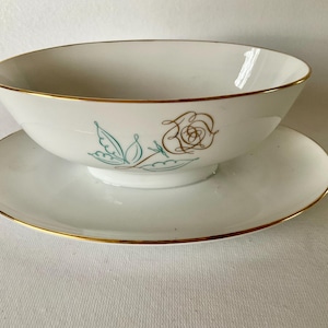 May include: White porcelain bowl and saucer set with gold trim. The bowl features a floral design in gold and teal. The saucer is round with a gold rim. A classic vintage tableware set.