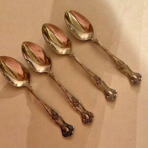 May include: Four silver spoons with ornate handles. The spoons have a rounded bowl and a decorative design of grapes and leaves.
