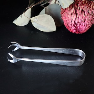 Puede incluir: Pinzas de azúcar de plata con un diseño curvo y la inscripción 'Made in England'.