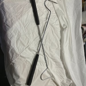 May include: A metal hook with a black handle and a long, curved end. The hook is designed for retrieving items from hard-to-reach places.