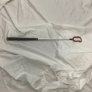 May include: A silver and black golf club with a red and black rubber grip. The club has a loop at the end of the shaft.