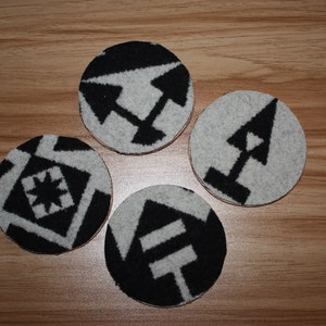 May include: Four round black and white coasters with different geometric patterns. The coasters are made of a soft, fuzzy material.