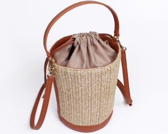 May include: A brown woven bucket bag with a brown leather strap and a drawstring closure. The bag has a beige fabric lining.