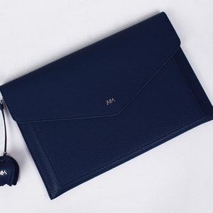May include: A dark blue leather envelope clutch with a silver zipper and a small charm with the initials "MM" on it.