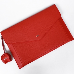 May include: A red leather envelope clutch with a small red leather tassel. The tassel has the letters "M.A." embossed on it.