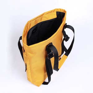 May include: A yellow tote bag with black straps and buckles. The bag is open and the inside is lined with black fabric.