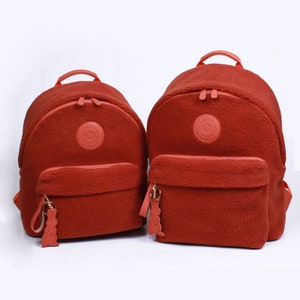 May include: Two red fleece backpacks with a round logo and a fuzzy keychain.
