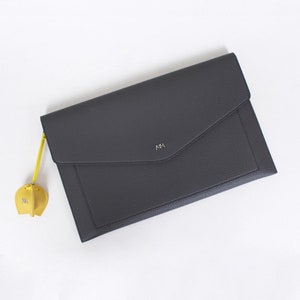 May include: A gray leather envelope clutch with a small yellow leather elephant charm attached. The clutch has a flap closure and the initials "MM" are embossed on the front.
