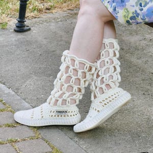 May include: Off-white crochet leg warmers with matching sneakers. The leg warmers feature an open, geometric design and extend to the mid-calf. The sneakers have a low profile and the word "CHIQUE" is printed on the side.
