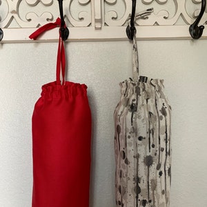 May include: Two reusable grocery bags hanging on hooks. One bag is red and the other is beige with black paint splatters.