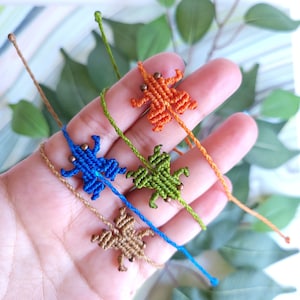 May include: Four friendship bracelets with different colored woven animal figures. The bracelets are brown, green, blue, and orange. Each bracelet has a small bead at the end.