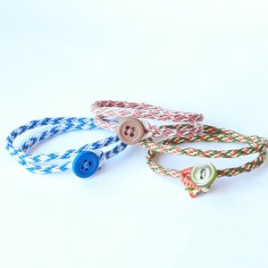 May include: Three braided bracelets with button closures. One bracelet is white and blue, one is red and white, and one is green and white.