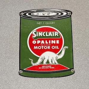 May include: A vintage Sinclair Opaline Motor Oil sign. The green can-shaped sign features a red and white Sinclair logo, the text "NET 1 QUART", and a white dinosaur illustration. The sign reads "MELLOWED 80 MILLION YEARS".
