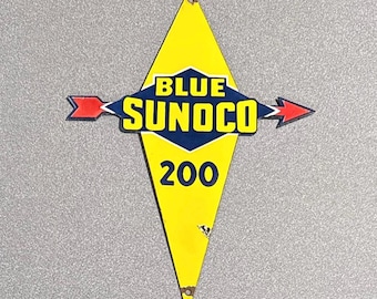 Puede incluir: Letrero vintage amarillo y azul Sunoco 200. El letrero tiene forma de diamante con las palabras "BLUE SUNOCO" en un diseño azul y amarillo. Flechas rojas apuntan a izquierda y derecha. El número "200" es azul.