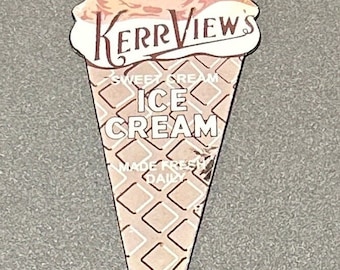 Può includere: Un cartello vintage in metallo a forma di cono gelato. Il cartello è rosa e bianco con lettere marroni. Dice "Serving Kerrview's Sweet Cream Ice Cream Made Fresh Daily".