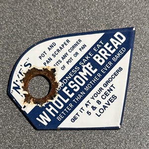 May include: Vintage metal pot and pan scraper with a hole for hanging. The scraper is white and blue with text that reads "Wholesome Bread" and "Better Than Mother Ever Baked".