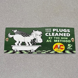 May include: Vintage green and white AC spark plug advertisement. The image features a cartoon horse in a bathtub with the text "Have Your Plugs Cleaned by the New AC Method". The AC logo is also visible.