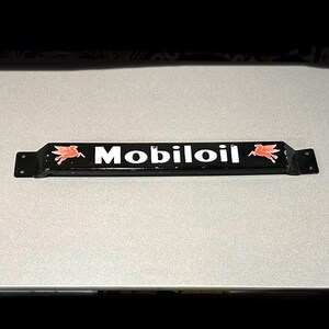 May include: Black metal sign with white lettering that reads "Mobiloil". The sign has two red flying horse logos on either side of the text.
