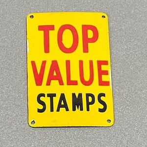 Puede incluir: Un letrero de metal amarillo con texto negro y rojo que dice "TOP VALUE STAMPS".