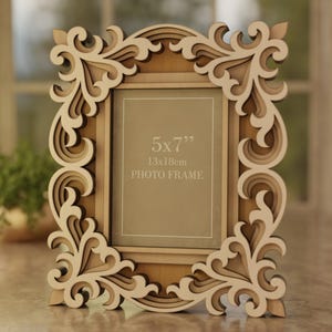 May include: A decorative wooden photo frame with an ornate, layered design. The frame is light brown with cream-colored accents and features the text "5x7" 13x18cm PHOTO FRAME". The frame is designed to hold a 5x7 inch photo.