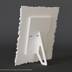 Pu&ograve; includere: Una cornice bianca con un bordo smerlato decorativo e un cavalletto integrato. La cornice &egrave; realizzata in un materiale solido e opaco ed &egrave; progettata per stare in posizione verticale. Il retro della cornice presenta un design geometrico semplice.