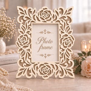 May include: A rectangular light-colored wooden photo frame featuring an intricate laser-cut border with floral rose motifs and swirling leaf patterns. The center of the frame contains a white insert with the text Photo frame in cursive script.