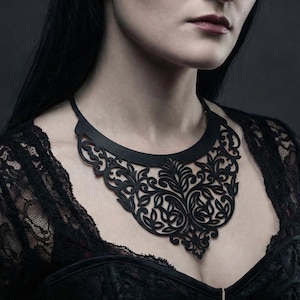 May include: A black laser-cut necklace template with an ornate floral pattern. The necklace is worn by a person in a black lace top. The image includes the text "Laser Cut Necklace Template" at the top.