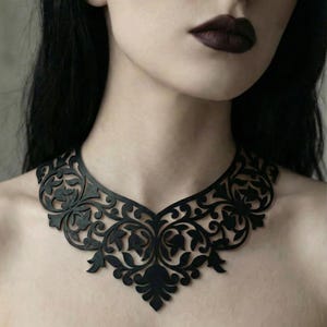 Puede incluir: Un patrón de collar negro cortado con láser con un intrincado diseño floral. El collar se lleva alrededor del cuello. El texto "Laser Cut Necklace Template" está en la parte superior de la imagen.