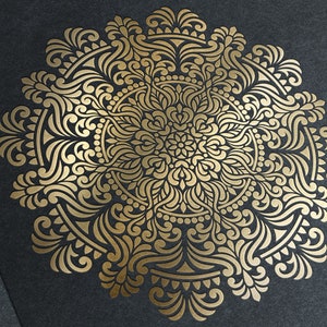 May include: A gold mandala design with intricate details and a floral pattern. The mandala is on a dark grey background.