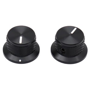 May include: Two black cylindrical control knobs with a knurled texture on the sides for grip. Each knob features a flat top surface with a single white indicator line and a wide, smooth circular base. One knob shows a small side set screw.