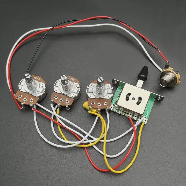Op de afbeelding: Gitaarbedradingscomponenten, waaronder drie potentiometers, een schakelaar en een jack. De potentiometers hebben bruine bases en zilveren knoppen, verbonden door rode, witte en gele draden. De schakelaar is groen en wit, met een zwarte tuimelschakelaar.