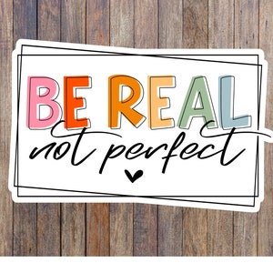 Puede incluir: Una pegatina blanca con borde negro y el texto "BE REAL not perfect" en letras de colores. El texto está escrito a mano con un símbolo de corazón debajo.