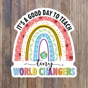 May include: A colorful rainbow sticker with a ruler, pencils, and paper clips. The text "IT'S A GOOD DAY TO TEACH tiny WORLD CHANGERS" is written on the sticker.