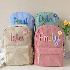 Può includere: Quattro zaini in velluto a coste dai colori pastello: azzurro, verde, beige e rosa. Ogni zaino ha un nome ricamato: Paul, Dylan, Isla ed Emily. Sono presenti anche piccoli fiori decorativi.