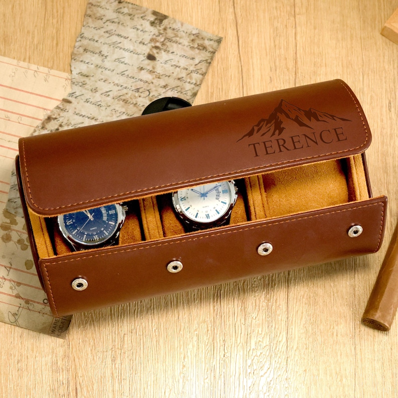 May include: A brown leather watch case with three compartments, each holding a wristwatch. The case has a mountain graphic and the name "TERENCE" engraved on the flap. The case is closed with three snap closures.