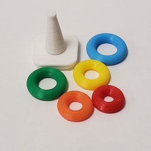 May include: A white cone-shaped stacking toy with five colorful rings. The rings are green, yellow, orange, red, and blue.