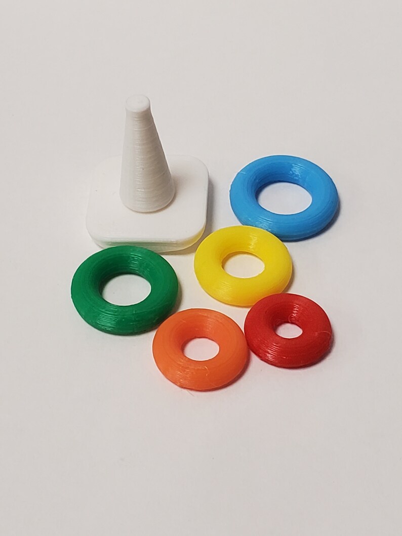 May include: A white cone-shaped stacking toy with five colorful rings. The rings are green, yellow, orange, red, and blue.